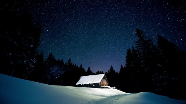 Time-lapse. Beautiful wooden house in the winter forest under the stars