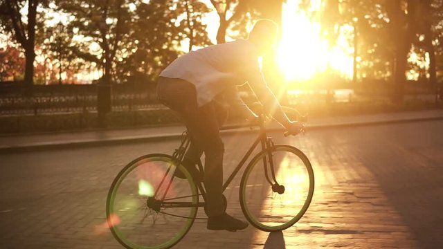 Happy young man riding bicycle on empty bike road through green tree park on summer sunny day in the morning