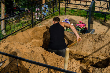 grave-digger digs a grave, a man digs a grave with a shovel in a cemetery - obrazy, fototapety, plakaty