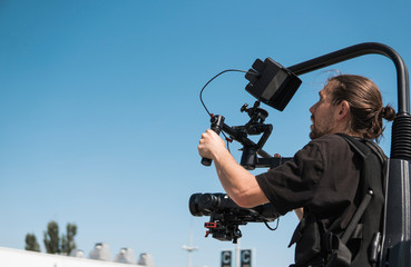 Professional videographer holding camera on 3-axis gimbal which mounted on easy rig. Videographer using steadicam. Pro equipment helps to make high quality video without shaking.