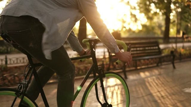 Close up footage of a man cycling a bicycle in the morning park or boulevard. Side view of a young man riding a trekking bike. Sun shines on the background