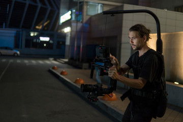Professional videographer holding camera on 3-axis gimbal which mounted on easy rig. Videographer using steadicam. Pro equipment helps to make high quality video without shaking. © Volodymyr_sh