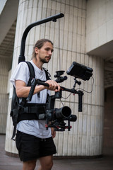 Fototapeta na wymiar Professional videographer holding camera on 3-axis gimbal which mounted on easy rig. Videographer using steadicam. Pro equipment helps to make high quality video without shaking.