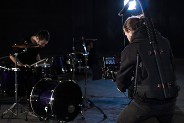 Professional videographer holding camera mounted on easy rig and filming a drummer. Videographer using steadicam. Pro equipment helps to make high quality video without shaking. © Volodymyr_sh