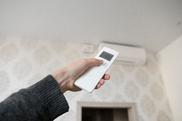Hand with remote control directed on the conditioner on the wall. Man's hand using remote control open The air conditioner is cooled to 25 degrees Celsius in his bedroom.