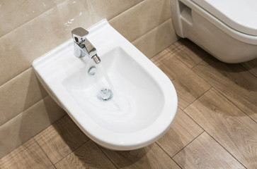 Details of white ceramic bidet with a running water in modern bathroom.