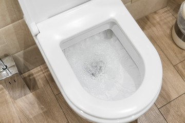 White toilet bowl in a bathroom. Closeup view of a flushing white toilet. The water swirls in the...