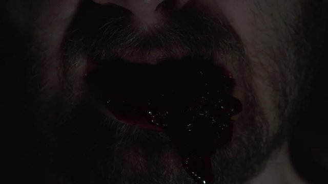 Creepy man zombie, cannibal furiously eating raw meat with frenzy. Blood drips from the mouth. Horror, halloween concept