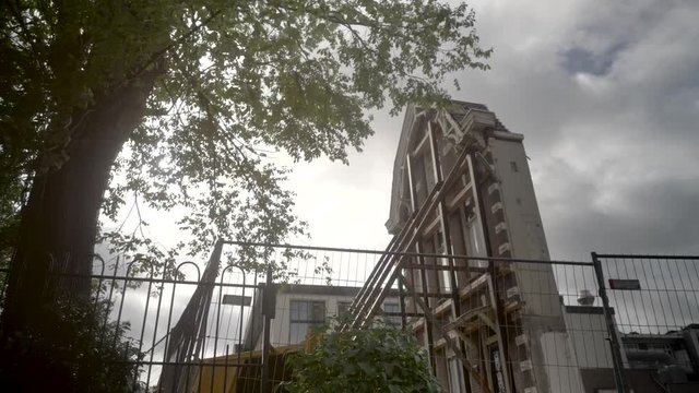 An old Fenced off Derelict House in Amsterdam, With Trees Swaying in the Foreground  and Cloudy Skies Passing Over the Building.