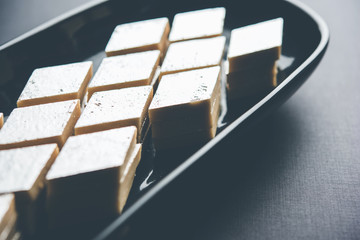 Kaju Katli is a Diamond shape Indian sweet made using cashew sugar and mava, served in a plate or bowl over moody background. selective focus