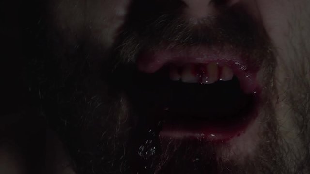 Creepy man zombie, cannibal furiously eating raw meat with frenzy. Blood drips from the mouth. Horror, halloween concept