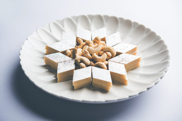 Kaju Katli is a Diamond shape Indian sweet made using cashew sugar and mava, served in a plate or bowl over moody background. selective focus