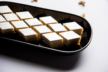 Kaju Katli is a Diamond shape Indian sweet made using cashew sugar and mava, served in a plate or bowl over moody background. selective focus