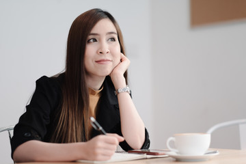 Asian woman working with laptop in coffee shop cafe,she thinking and holding pen