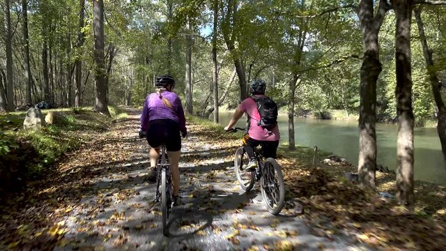 Mother and teenage son biking side by side on a rural gravel road with a river to their right side.