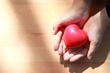 human hands holding red heart on wood