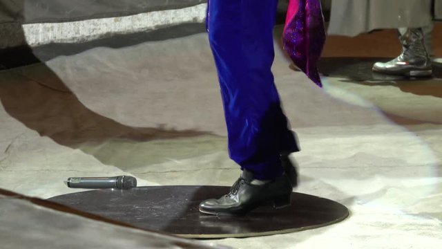 A clown tap dancer in blue pants showing various steps in circus arena close-up