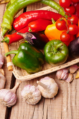 Cherry tomatoes, peppers, garlic, eggplants in a wicker basket. Fresh vegetables on a wooden table..