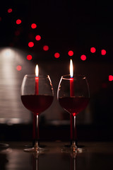 Romantic dinner: two glasses of wine and candels are in the dark with new year lights at the background