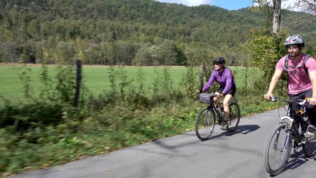 Mother and teenage son biking side by side on a rural road with farmland in the background.