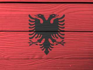 Flag of Albania on wooden wall background. Grunge Albanian flag texture, a red field with the black double-headed eagle in the center.