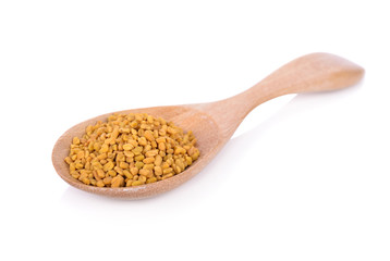 dry fenugreek seeds in wooden spoon on white background