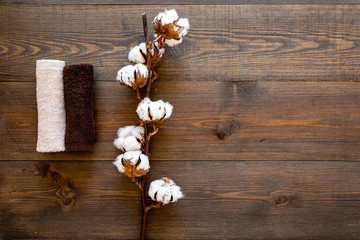 Spa concept. Set of towels twisted coil near cotton flowers on dark wooden background top view copy space