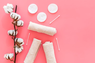 Cotton hygiene products. Cotton pads and swabs, towels twisted coil near dry cotton flowers on pink background top view copy space