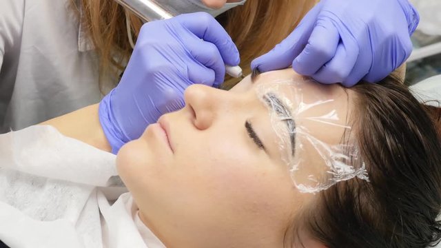 cosmetologist doing brows tattoo to female client. professional eyebrow permanent makeup. 4K