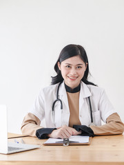 Female Asian doctor working at office desk and smiling at camera.