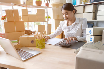 Asian woman entrepreneur using calculator with pencil in her hand, calculating financial expense at home office,online market packing box delivery,Startup successful small business owner,SME, concept