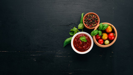 Traditional tomato ketchup sauce. Cherry tomatoes, spices, chili peppers, olive oil, parsley. Top view. On a black wooden background. Free space.