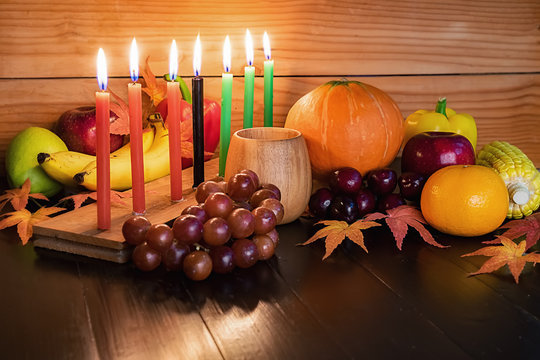 Kwanzaa holiday concept with decorate seven candles red, black and green, gift box, pumpkin,corn and fruit on wooden desk and background.