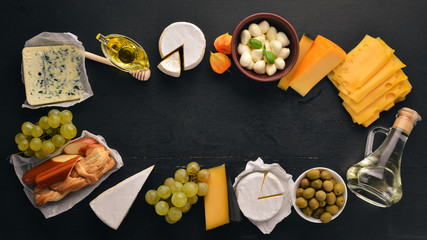A large set of cheeses. Mozzarella, blue cheese, brie cheese, maasdam. Top view. On a black wooden background. Free space for your text.