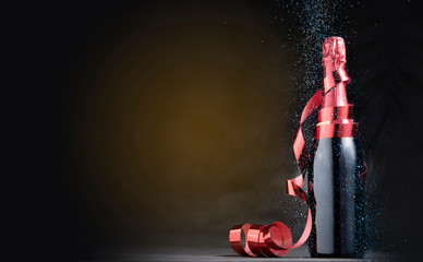 Red wine bottle with red ribbon and colored glitters over black background