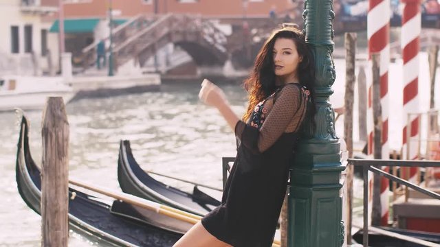 Seductive romantic woman standing on the pier against beautiful view on venetian chanal with boats and gondolas in Venice, Italy. Slow motion 4k footage. Gorgeous mixed race Asian Caucasian female in