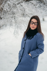 Portrait of happy young woman wearing winter hat and scarf stands next to the Christmas tree. black glasses