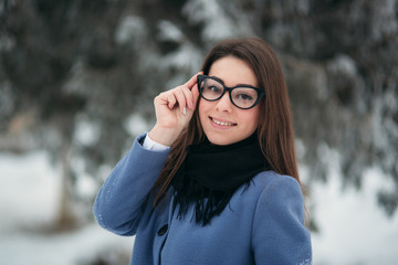 Portrait of happy young woman wearing winter hat and scarf stands next to the Christmas tree. black glasses