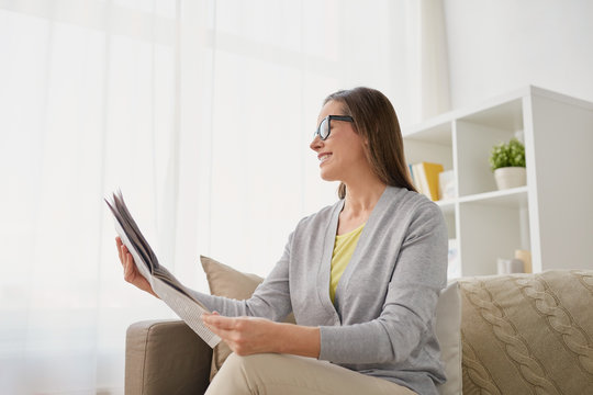 mass media and people concept - happy middle-aged woman reading newspaper at home