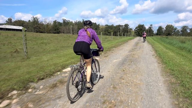 Following behind a woman biking with her son in the distance on a rural gravel road.