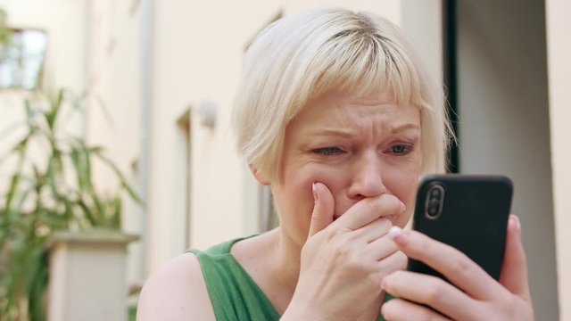 A pretty young blonde woman wearing a green dress sitting outside and using a phone. Close-up shot