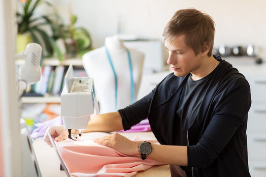 people, clothing and tailoring concept - fashion designer with sewing machine and cloth making new dress at studio