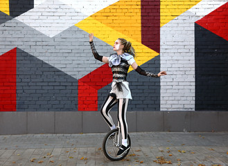 Girl clown performing with a unicycle - obrazy, fototapety, plakaty