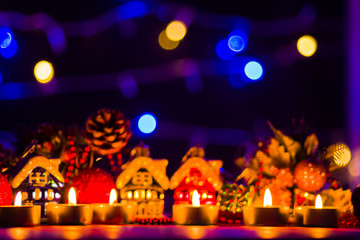 Merry Cristmas. Toy houses and candlelight. Christmas decorations on blurred background. Festive evening. Spruce branches and Christmas toys with bokeh. Copy space
