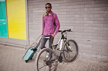 African american man in checkered shirt, sunglasses and jeans with suitcase and backpack. Black man traveler with bike.