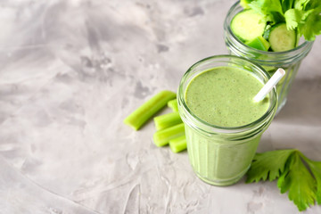 Jars with tasty green smoothie and cut vegetables on grey table