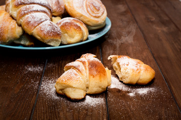 Halves of hot, ruddy buns with sugar on the background of a plate with pastries.