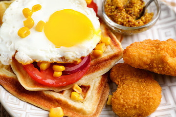 Delicious waffles with chicken nuggets, mustard and fried egg on plate, closeup