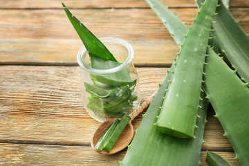 Jar and spoon with cut aloe vera leaves on wooden table
