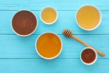Bowls with different types of honey and dipper on color wooden table